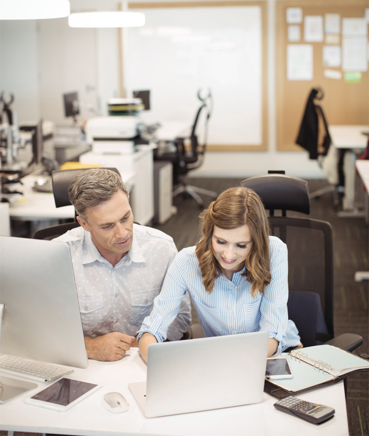 Office background with two co-workers looking at laptop